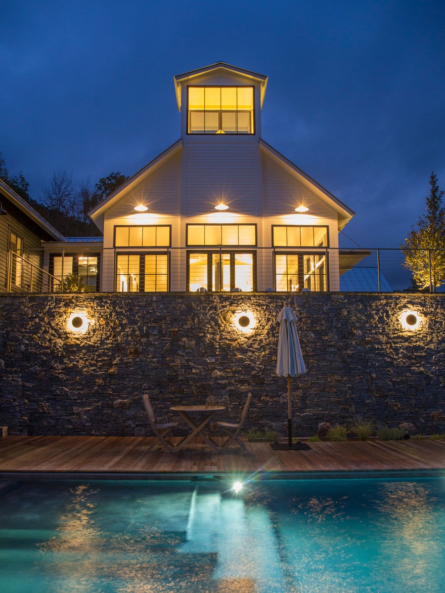 Poolside patio at night of home with black wood windows and patio doors in Williamstown, MA