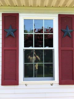 New vinyl double-hung window with traditional grille pattern and red shutters