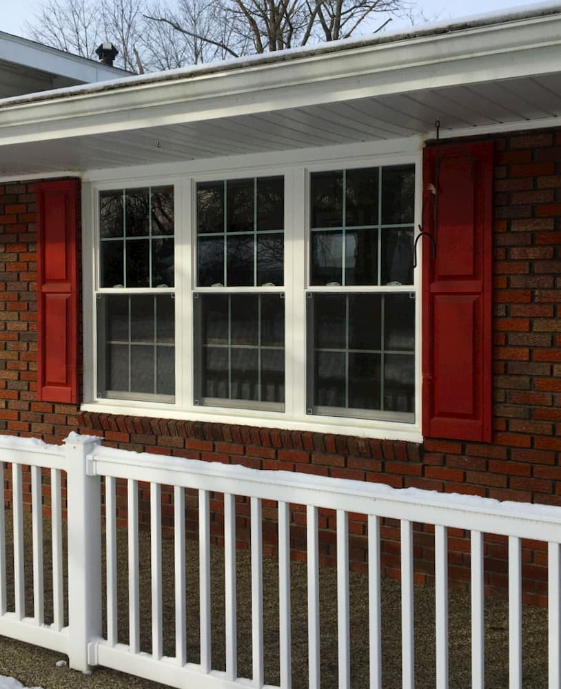 Three white double-hung vinyl windows framed by red shutters on a brick home