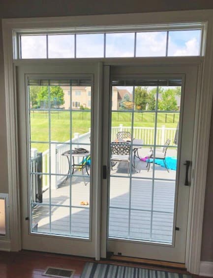 Interior view of new white wood sliding patio door with transom window and traditional grilles.