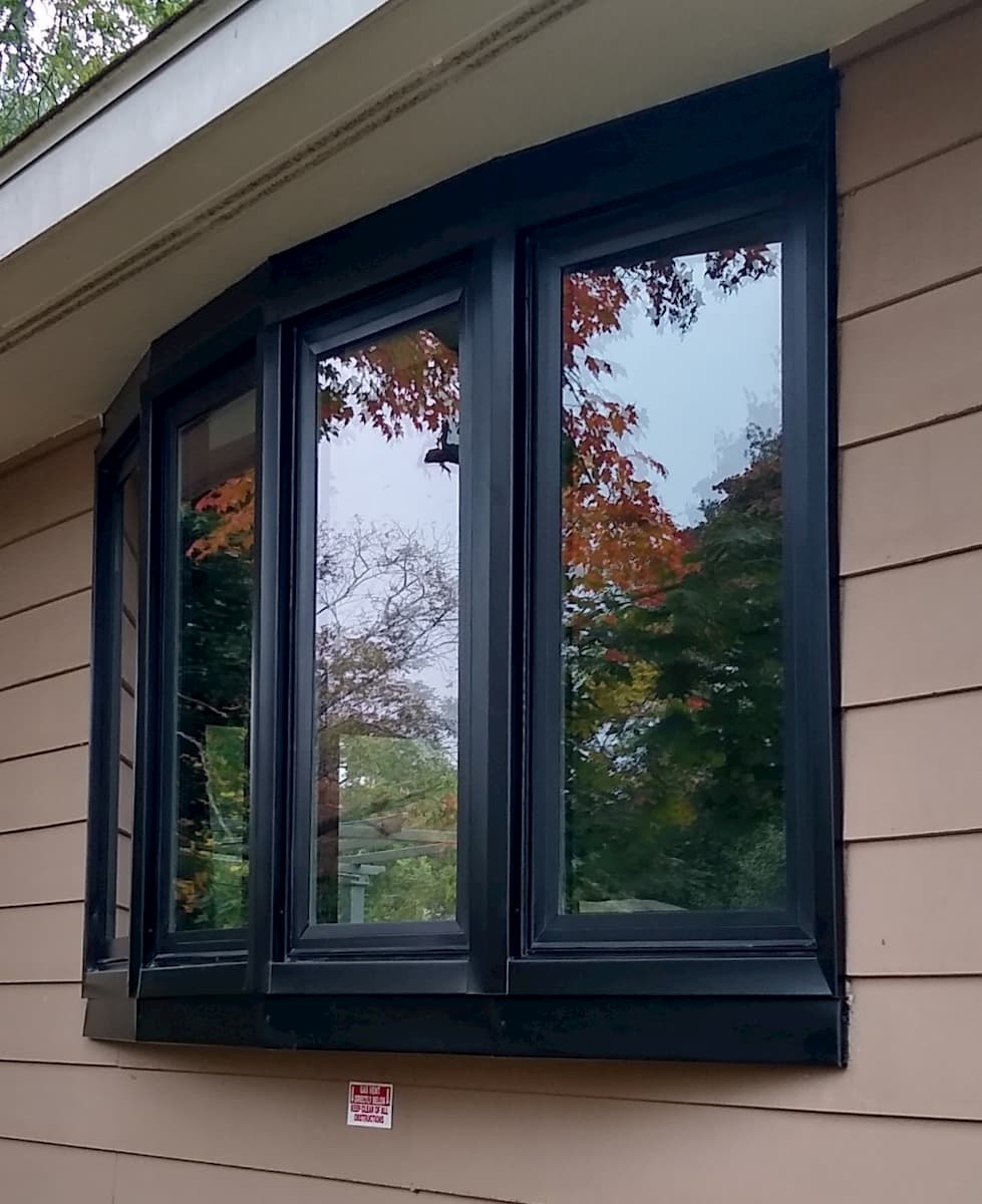Exterior view of black bow window on a home with brown siding.