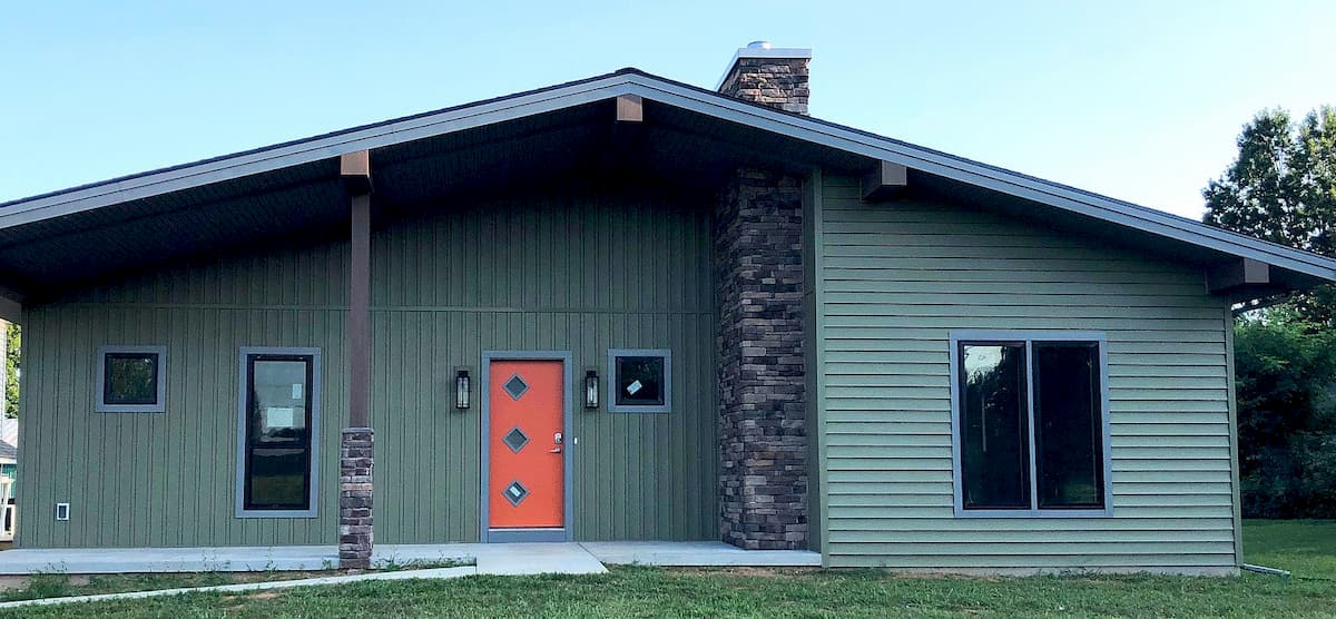 Front view of new green home with orange entry door and fiberglass casement windows
