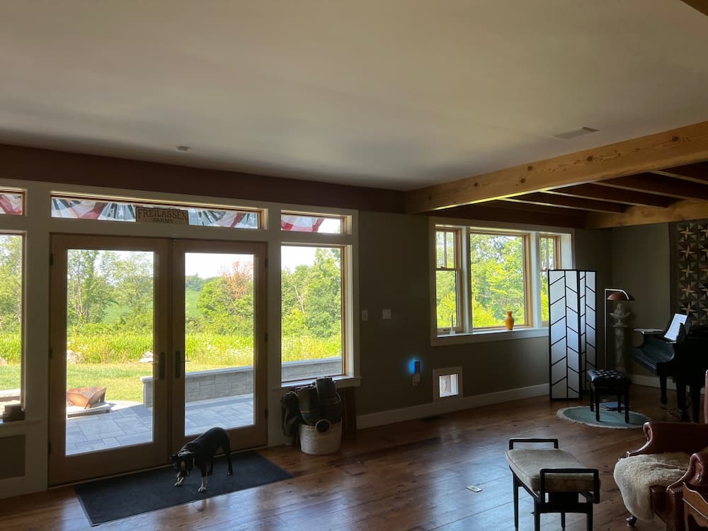 Interior view of living room natural wood windows and a hinged patio door overlooking yard
