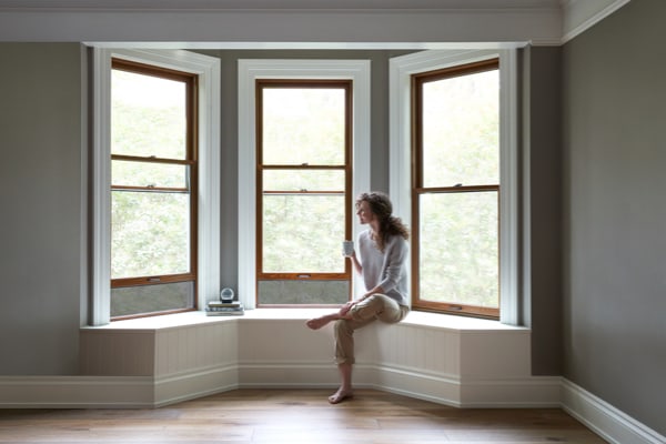 A woman sitting in the natural light of a bay window with a ledge 