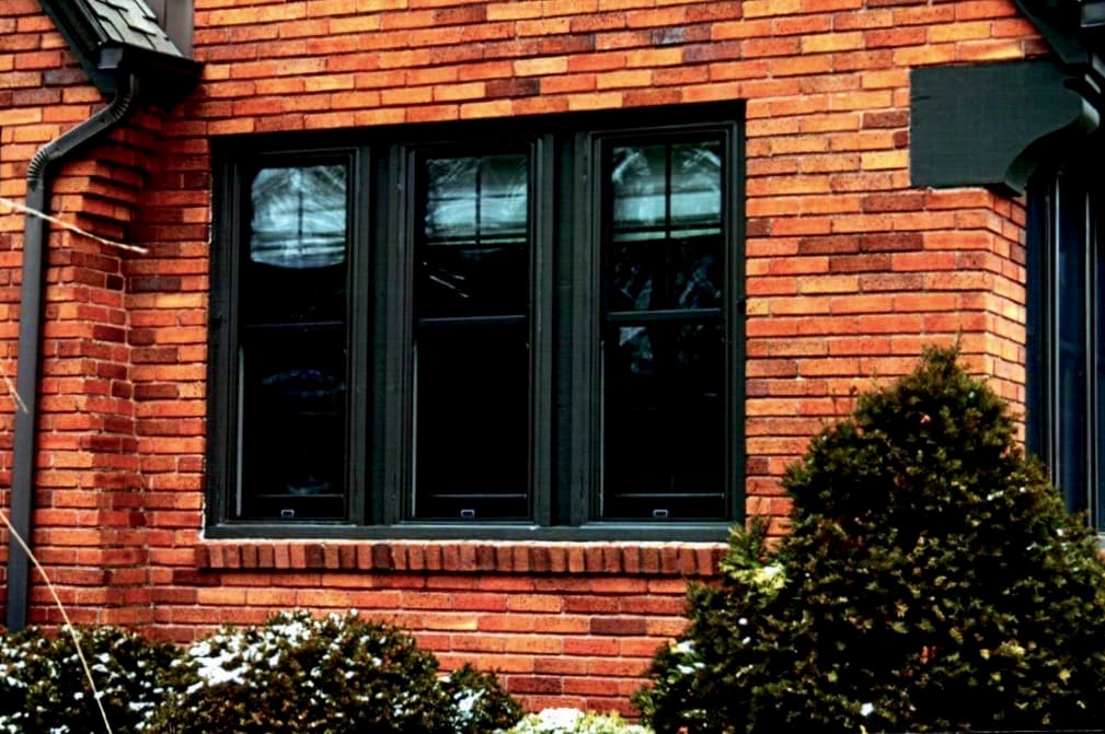 Exterior view of new wood double-hung windows against a red brick home.