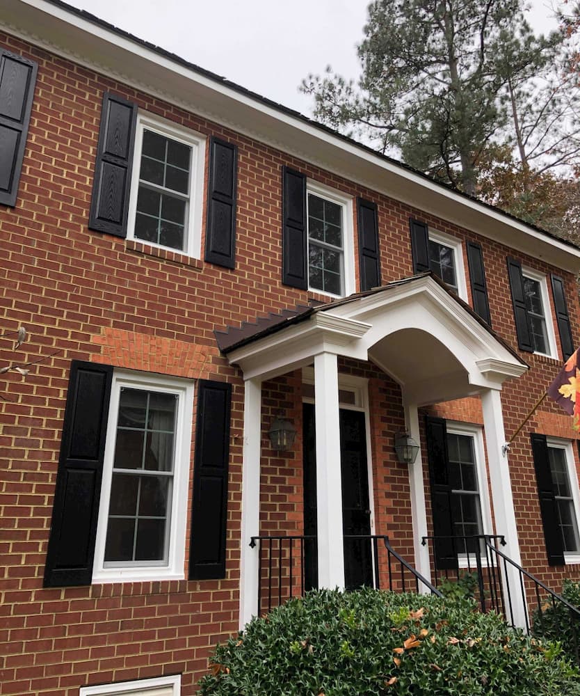 Exterior view of front entry of red brick home with new white vinyl double-hung windows