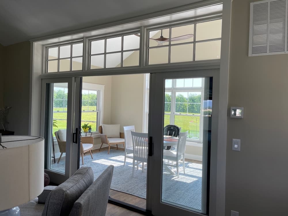 Sliding patio door featuring black hardware and white windows above it with grilles.