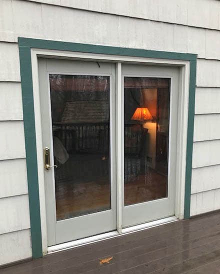 Exterior view of old hinged patio door on a home with white shingles.