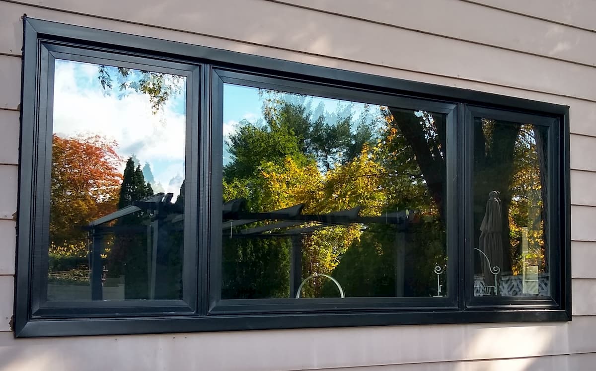 Exterior view of three black fiberglass windows on a home with brown siding.