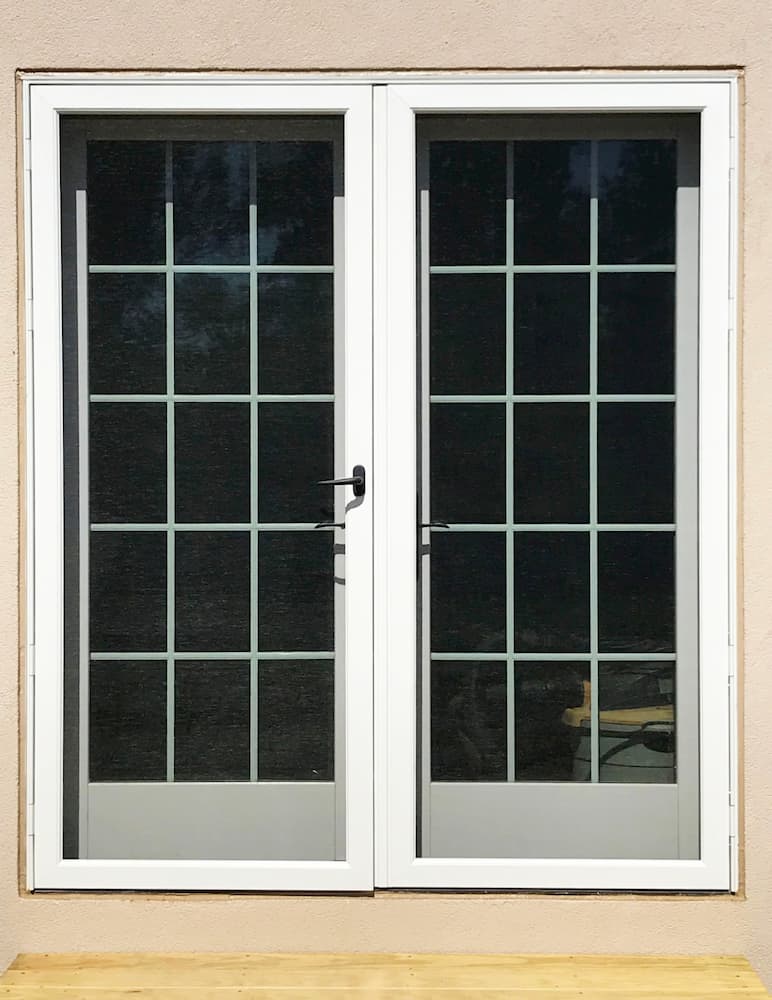 Exterior view of two white hinged French patio doors with traditional grille patterns