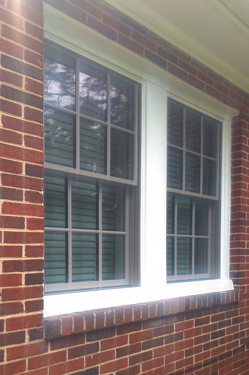Exterior view of white wood windows with traditional grilles on a red brick home