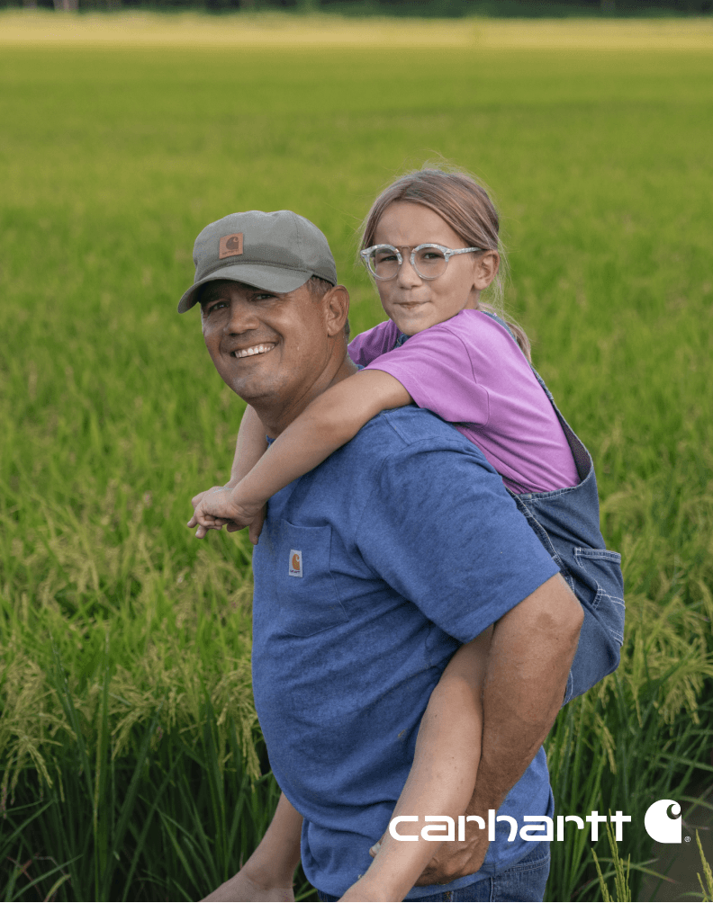 Adult carrying a child in a grassy field while wearing a casual Carhartt K87 t-shirt.