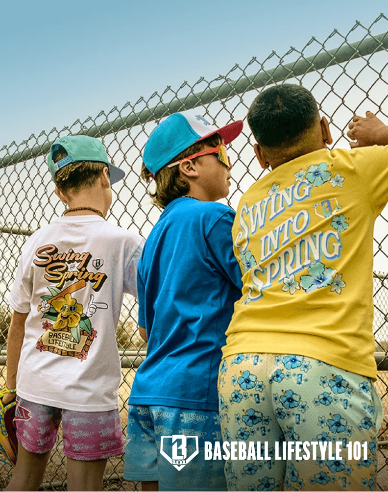 Three children standing along a chain-link fence wearing colorful Baseball Lifestyle 101 shirts and shorts.
