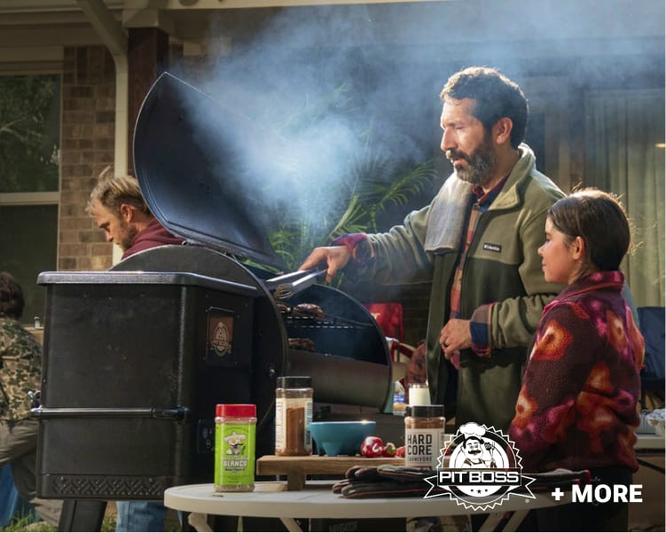 Outdoor Pit Boss pellet grill cooking food beside a campsite with cooking accessories and family members nearby.