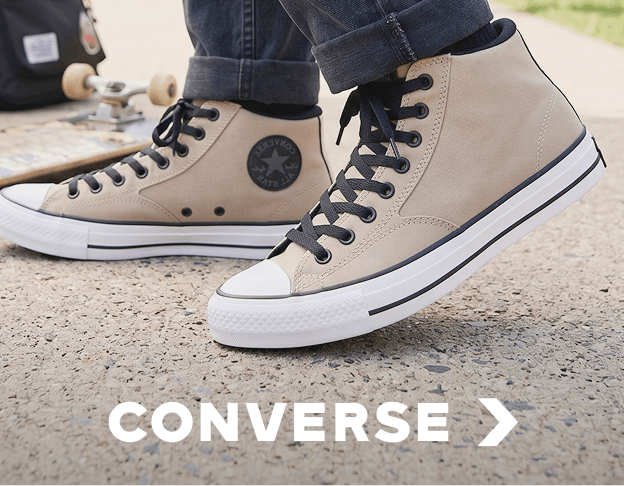 Close-up of beige Converse high-top sneakers on a sandy outdoor surface.