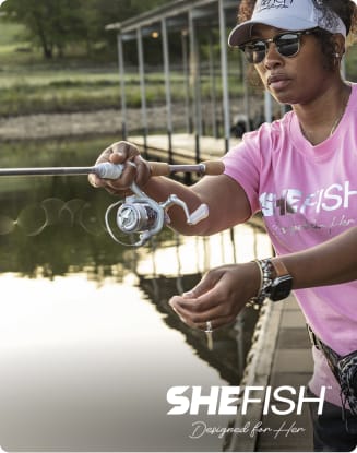 Person fishing from a dock while wearing casual outdoor apparel beside a lake.