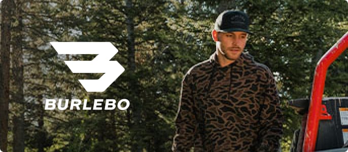 Person wearing a camouflage-pattern Burlebo pullover while standing outdoors near a pickup truck and wooded area.