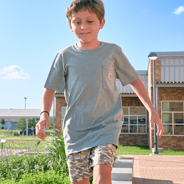 Kid walking outdoors in gray T-shirt and camo shorts for back-to-school.
