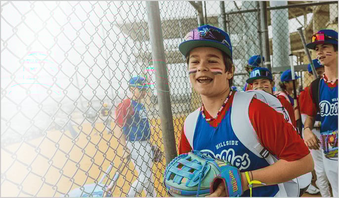 Youth baseball players in matching uniforms standing near a chain‑link fence, holding gloves and gear.