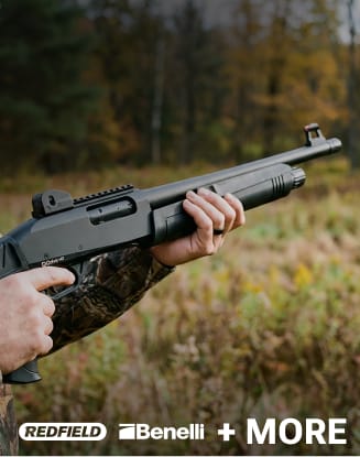 Person holding a shotgun in a wooded outdoor setting.