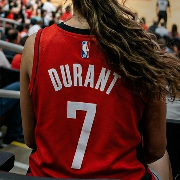 Back view of a red NBA basketball jersey showing the name DURANT and the number 7, worn in a basketball arena.