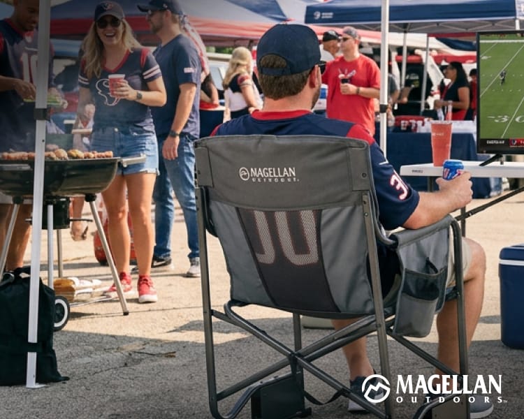 Outdoor tailgating setup featuring folding Magellan Outdoors Odyssey Rocker camp chairs, coolers, and a television showing a football game in a parking lot.