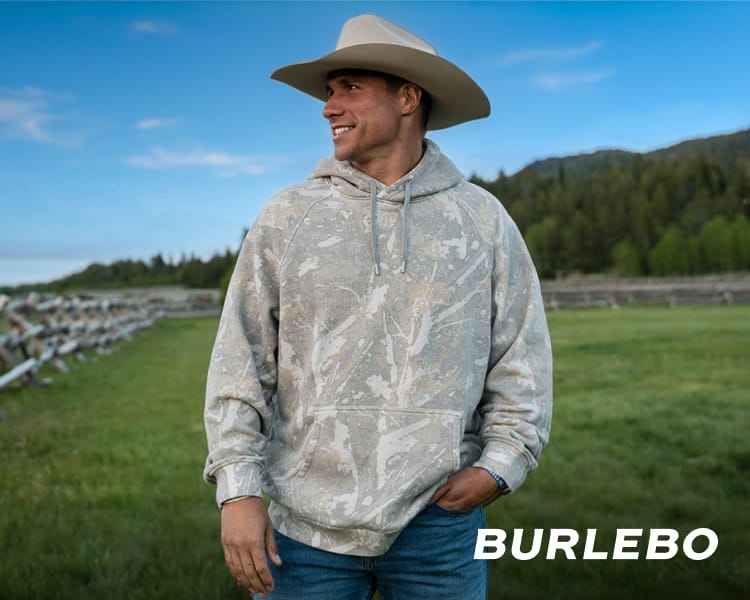 Person standing in a grassy outdoor setting wearing a Burlebo light washed camouflage hoodie.