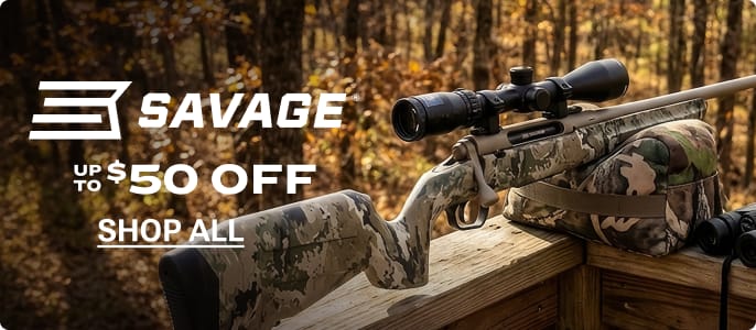 Savage rifle with mounted scope resting on a wooden shooting bench in a wooded outdoor setting.