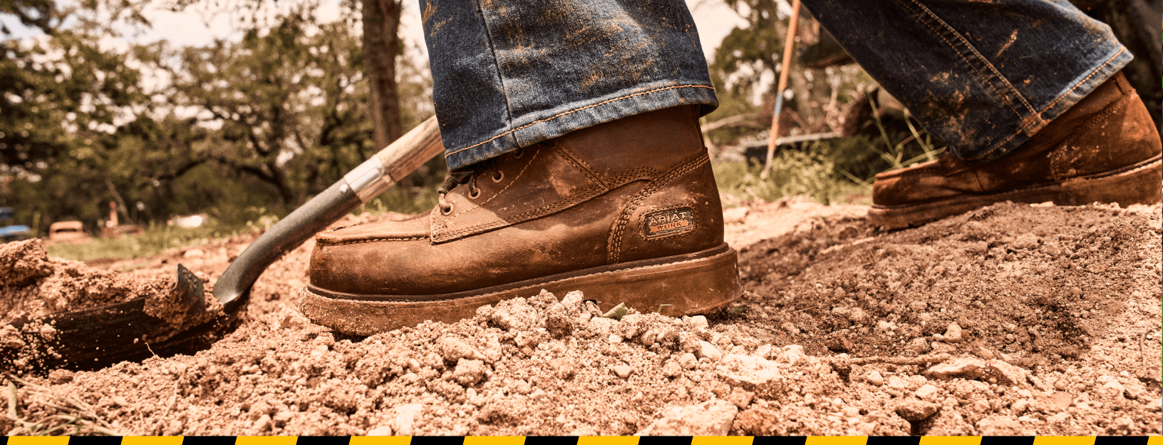 Close-up of durable brown Ariat work boots standing on muddy construction-site ground.