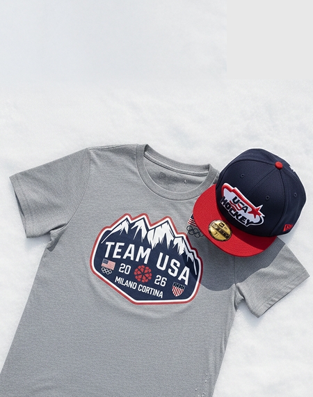 Gray Team USA Milano Cortina 2026 Winter Games T‑shirt displayed on a snow‑like background with a matching USA Hockey cap.