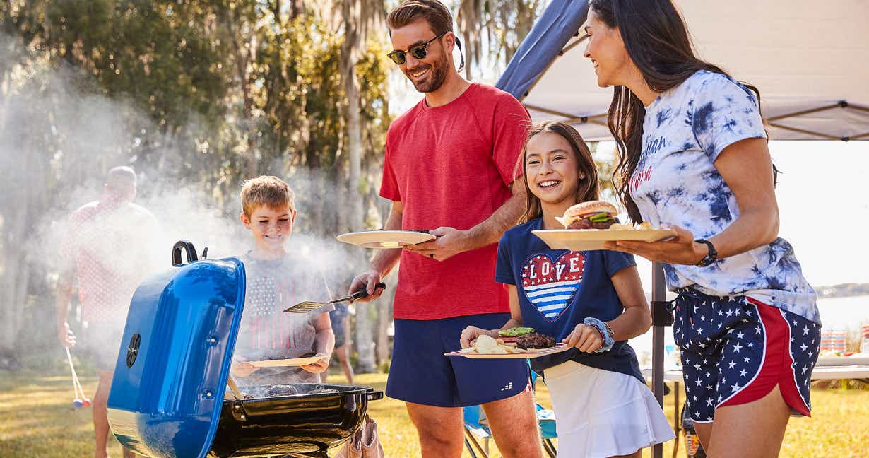Man serving burgers off the grill to his wife and children