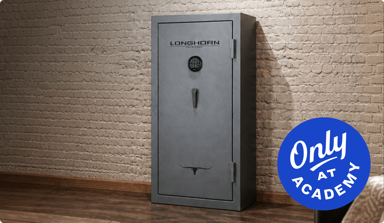 Large gray gun safe positioned against a white brick wall on a hardwood floor.