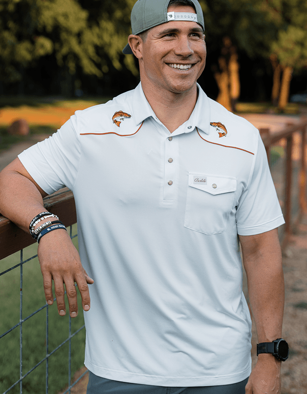 Person wearing a short sleeve snap performance polo shirt in light neutral color outdoors.