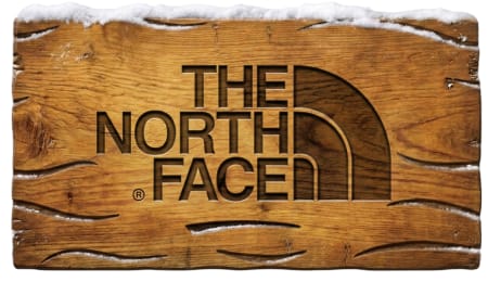 The North Face logo carved into a weathered wooden surface topped with snow.