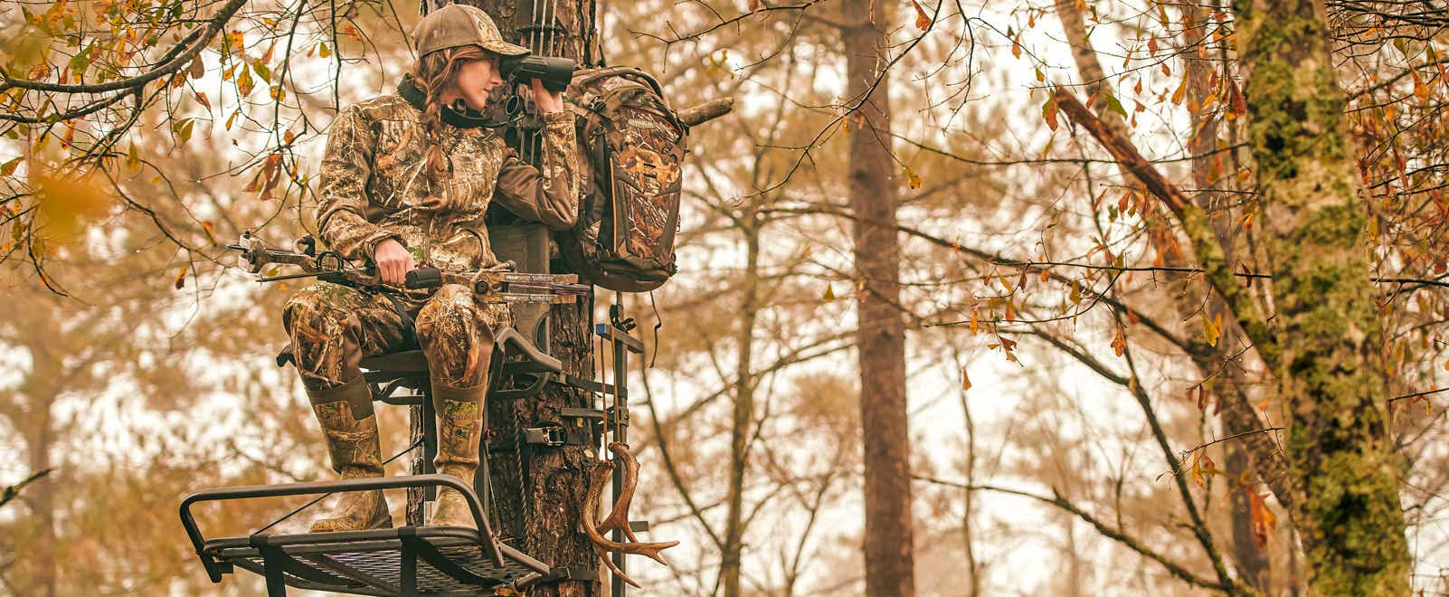 A hunter in a stand looking for deer with binoculars
