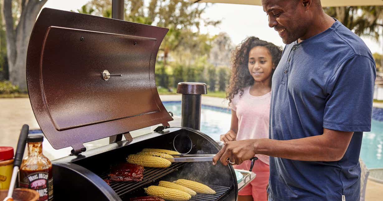 Man grilling some corn and beef in his smoker
