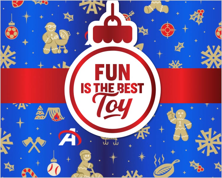 Holiday-themed Academy Sports + Outdoors graphic featuring a blue background with snowflakes, ornaments, gingerbread figures, candy canes, sports icons, and Academy “A” logos. A large red-and-white ornament in the center displays the text: “FUN IS THE BEST TOY.” A red ribbon runs horizontally behind the ornament.