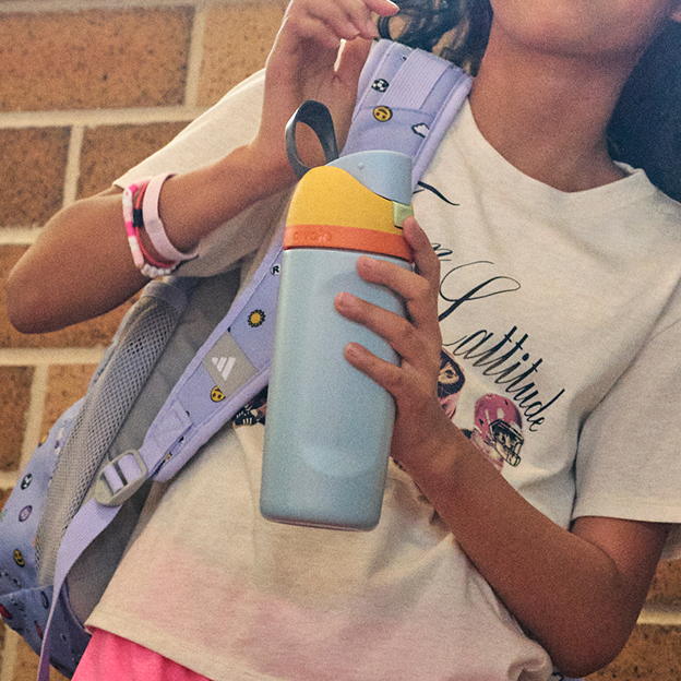Person holding reusable water bottle near backpack straps.