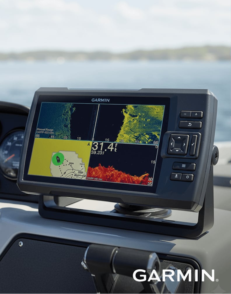 Garmin fish finder mounted on a boat console showing sonar and mapping screens, with water and shoreline in the background.