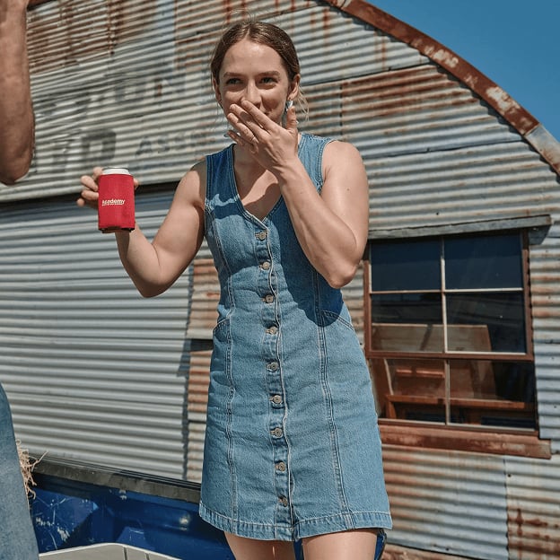 Person standing outdoors holding a red cup while wearing a sleeveless denim dress.