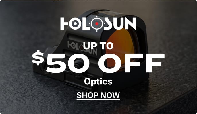 Hand holding a pistol equipped with a Holosun red dot sight at a shooting range. Holosun logo appears in the lower-right corner.