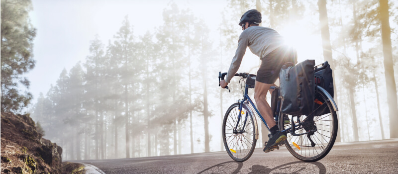 Cyclist on a bicycle with panniers riding along a foggy forest road