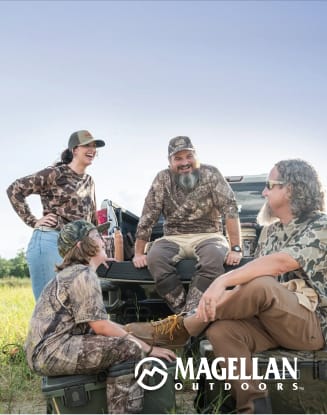 Group of four people wearing camouflage apparel gathered around the back of a vehicle in an open field.