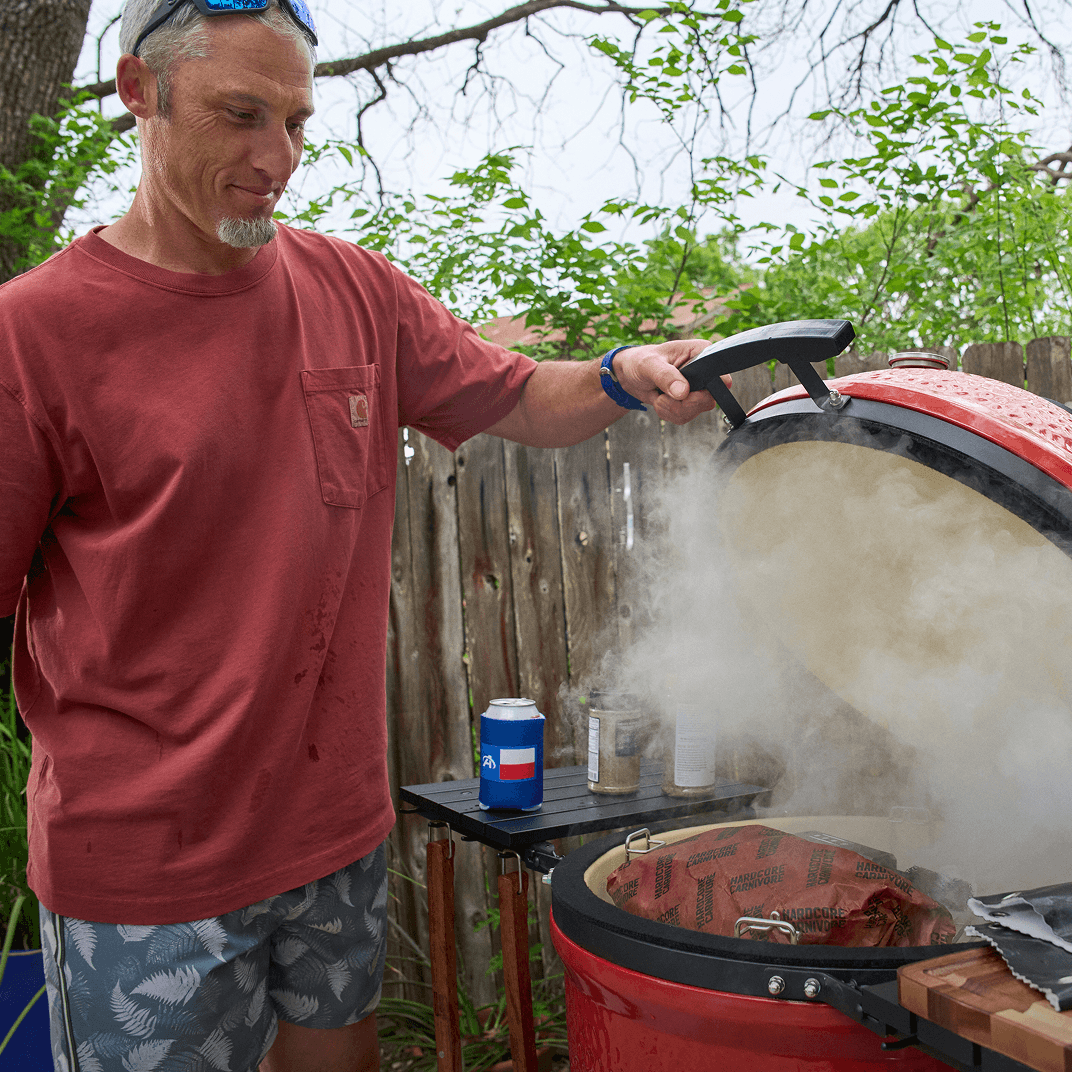 Outdoor smoker grill with food cooking and smoke rising from the lid.