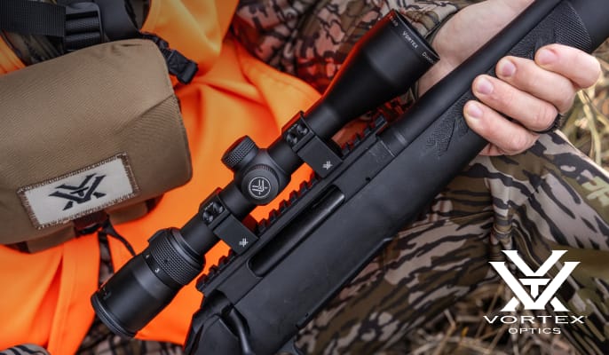 Rifle with mounted scope held by a hunter wearing camouflage apparel. Vortex logo appears in the lower-right corner.