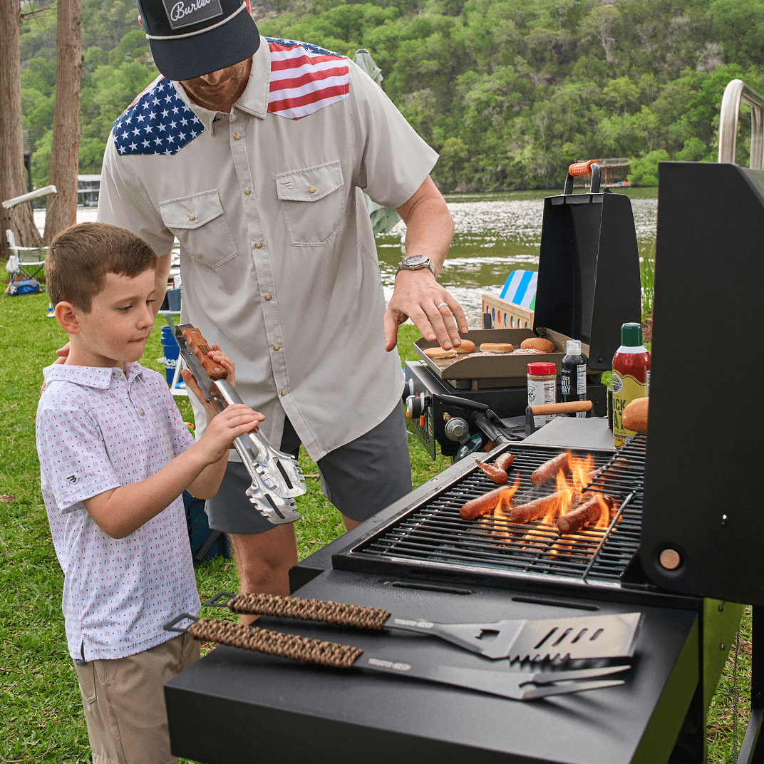 Gas grill cooking with open lid and visible flames during outdoor grilling.