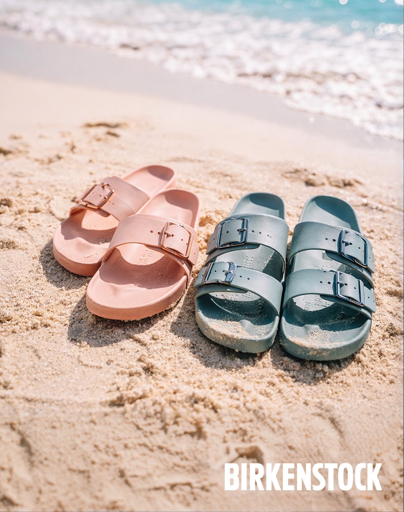 Two pairs of Birkenstock sandals—one pink and one teal—resting on sandy beach ground, showcasing comfortable family footwear.