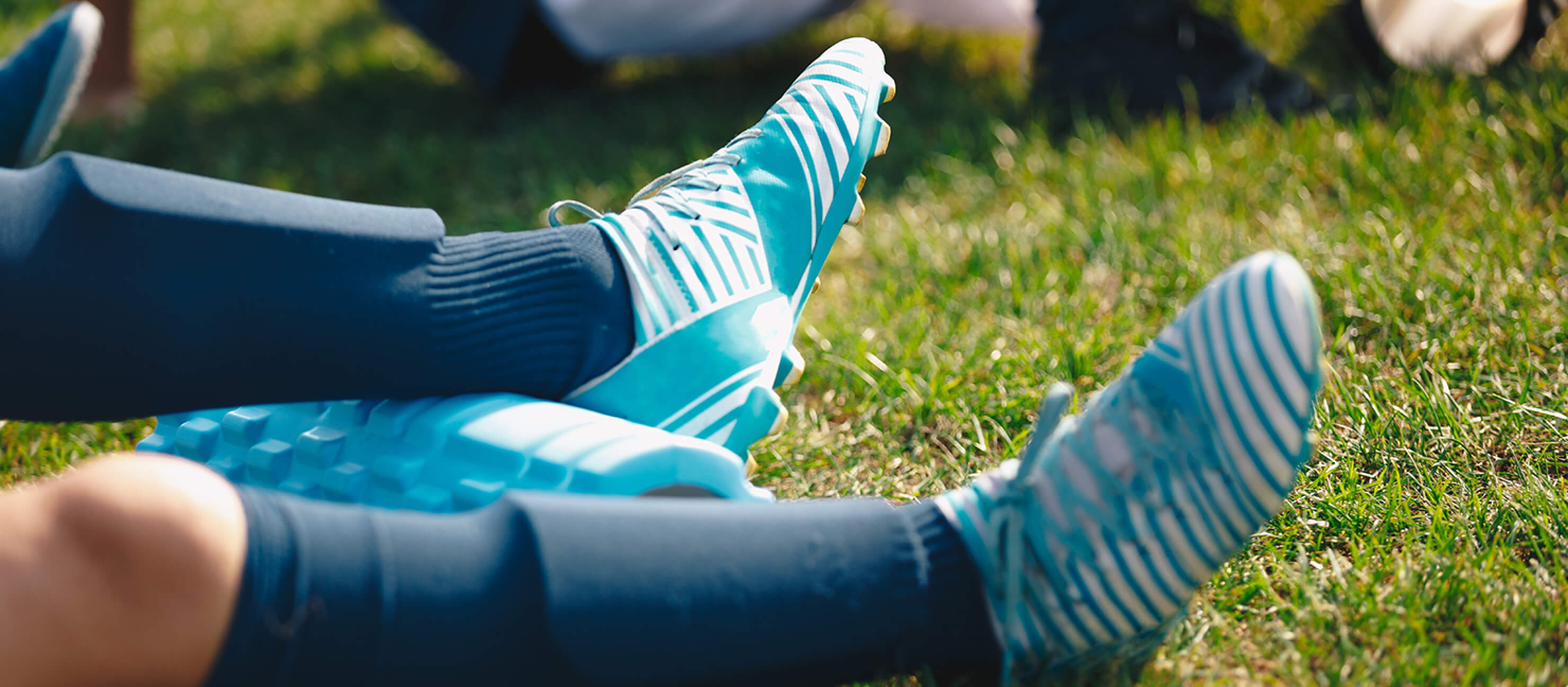Players wearing blue and white soccer cleats recover after practice using a foam roller