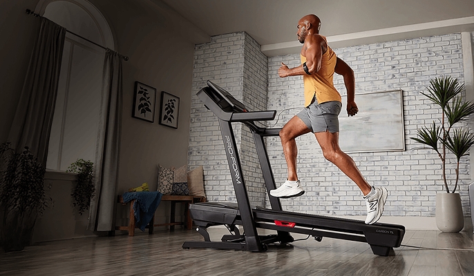 Person running on a treadmill in a modern living room with brick walls, plants, and framed pictures.