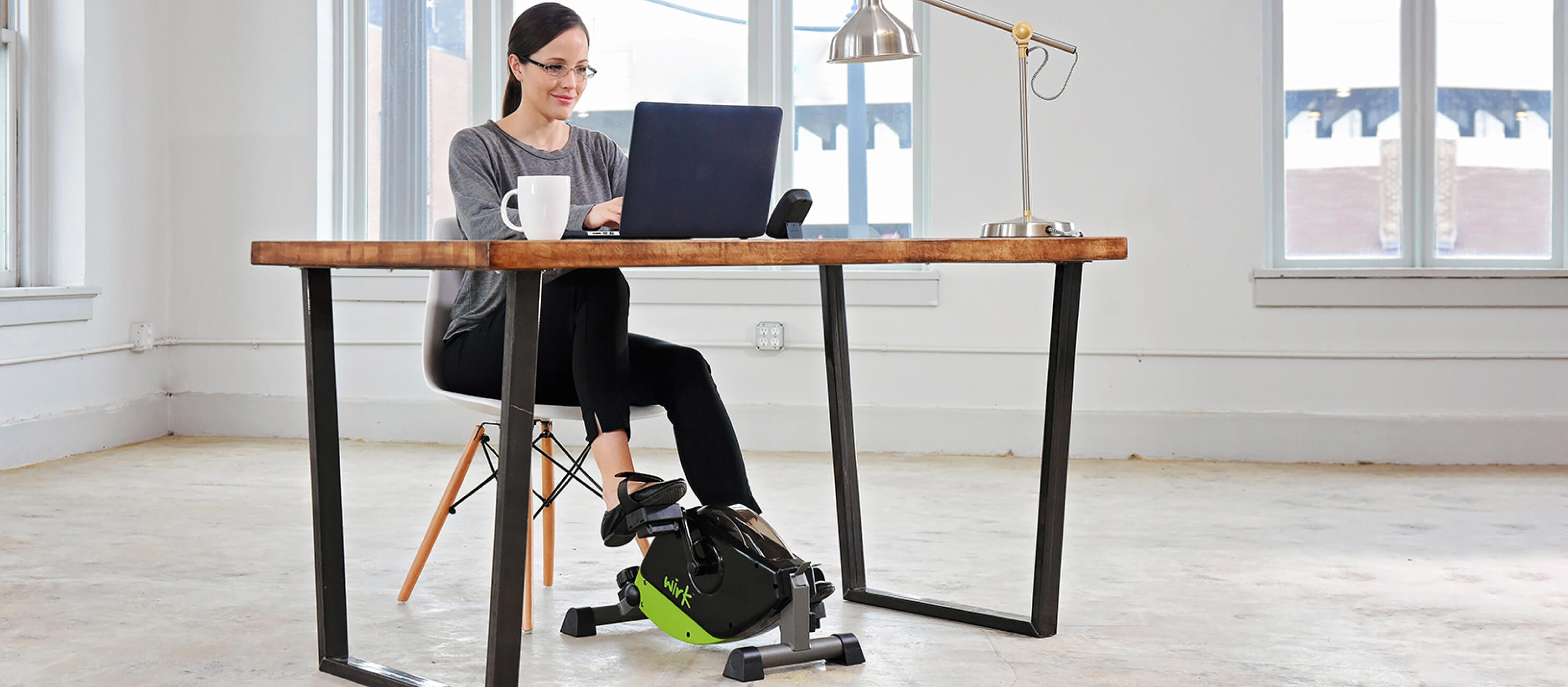 A woman works at her desk while pedaling on her mini exercise bike